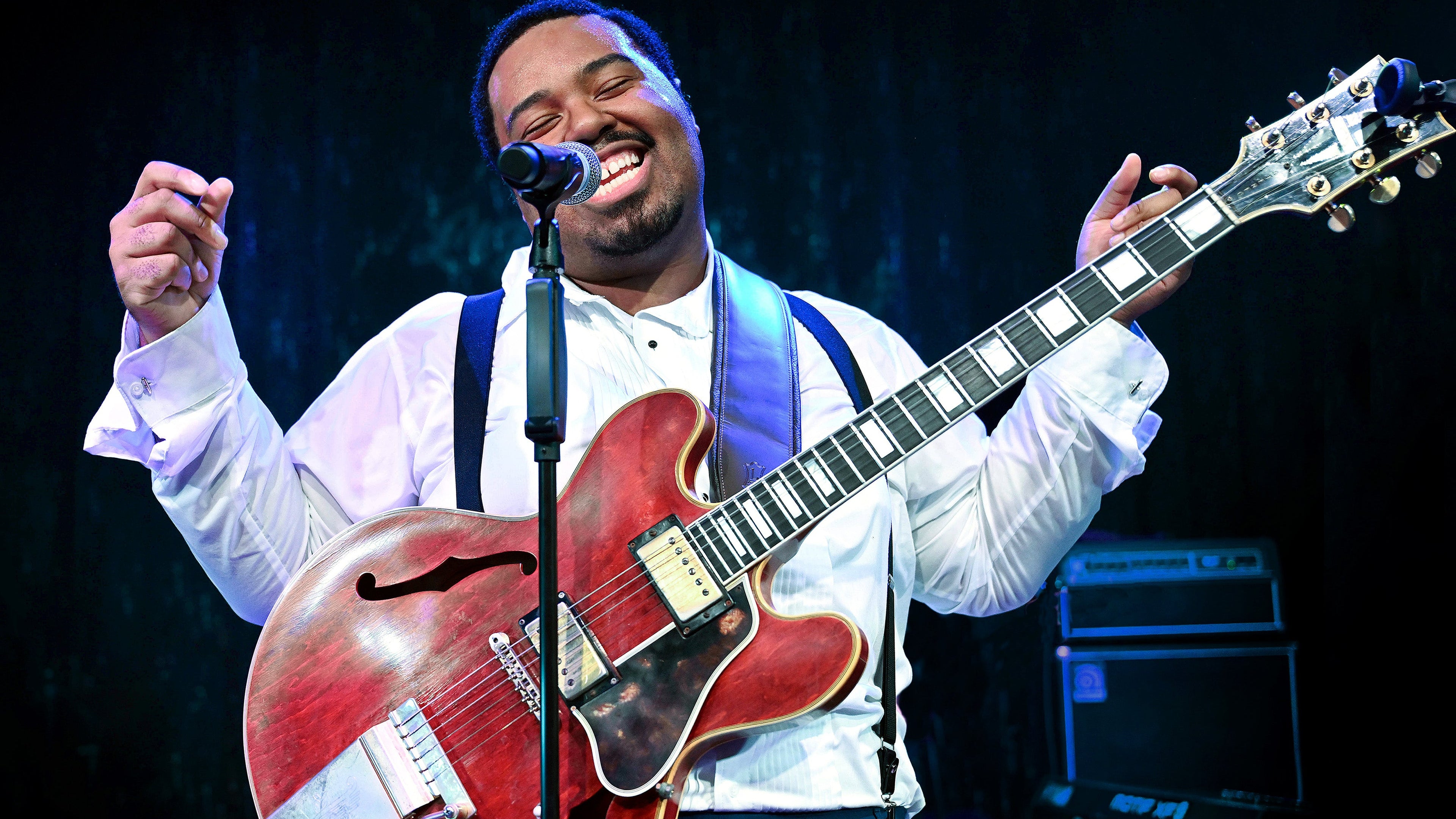 Man playing a red electric guitar on stage with a microphone